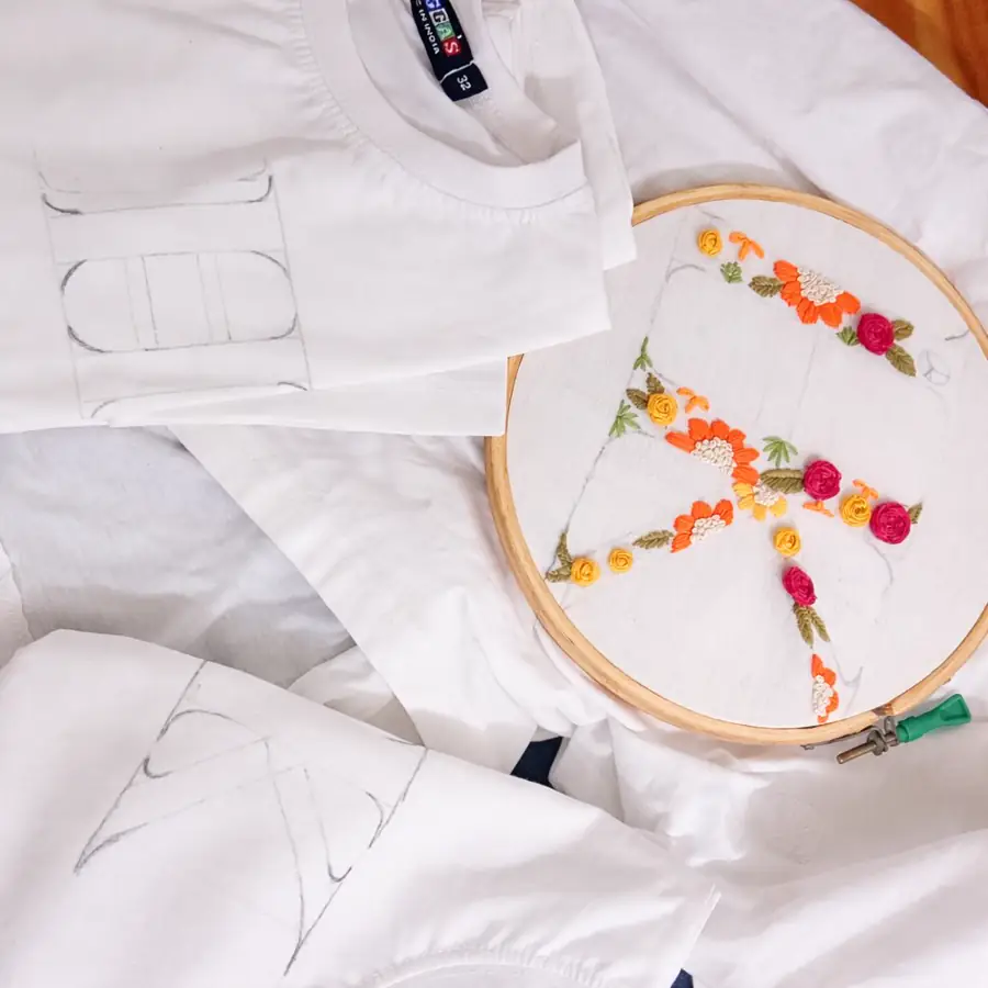 A floral initial being hand embroidered on a white tee in a hoop